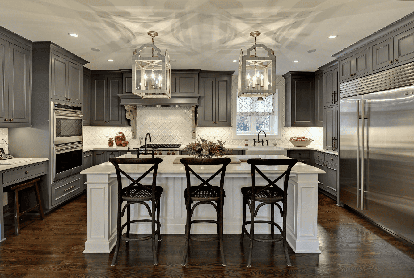 Modern kitchen with a large island and four bar stools under pendant lights.